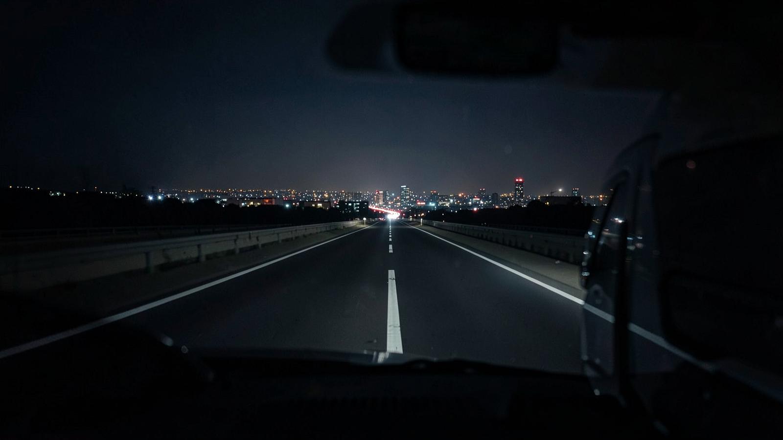 Empty highway at night seen from behind a delivery van, city lights in the distance