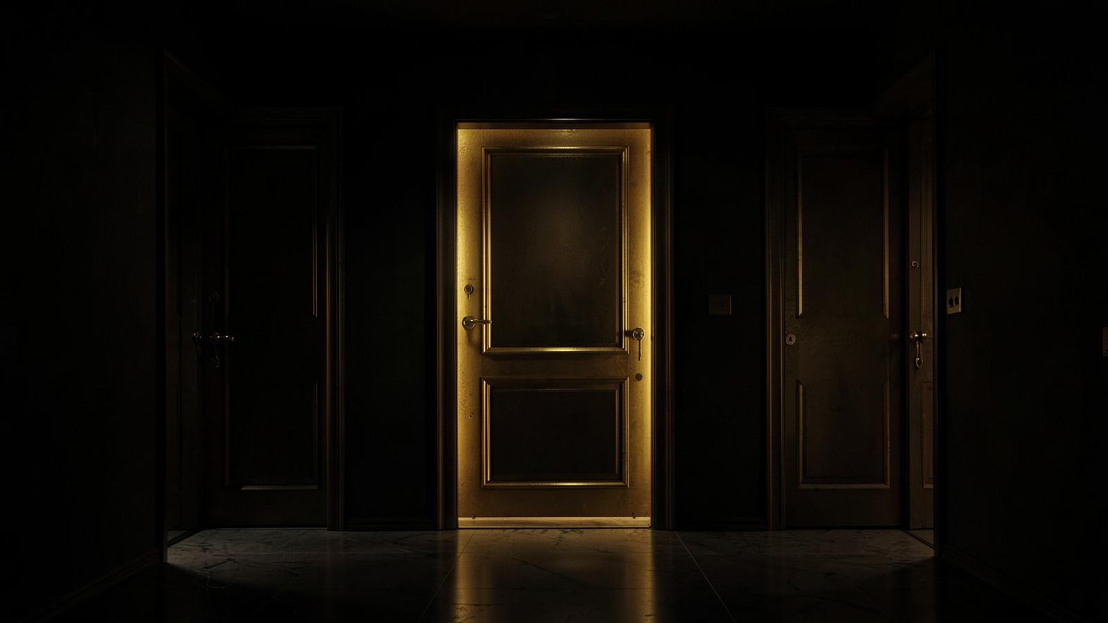 Three doors in a dark corridor with the center one lit in gold
